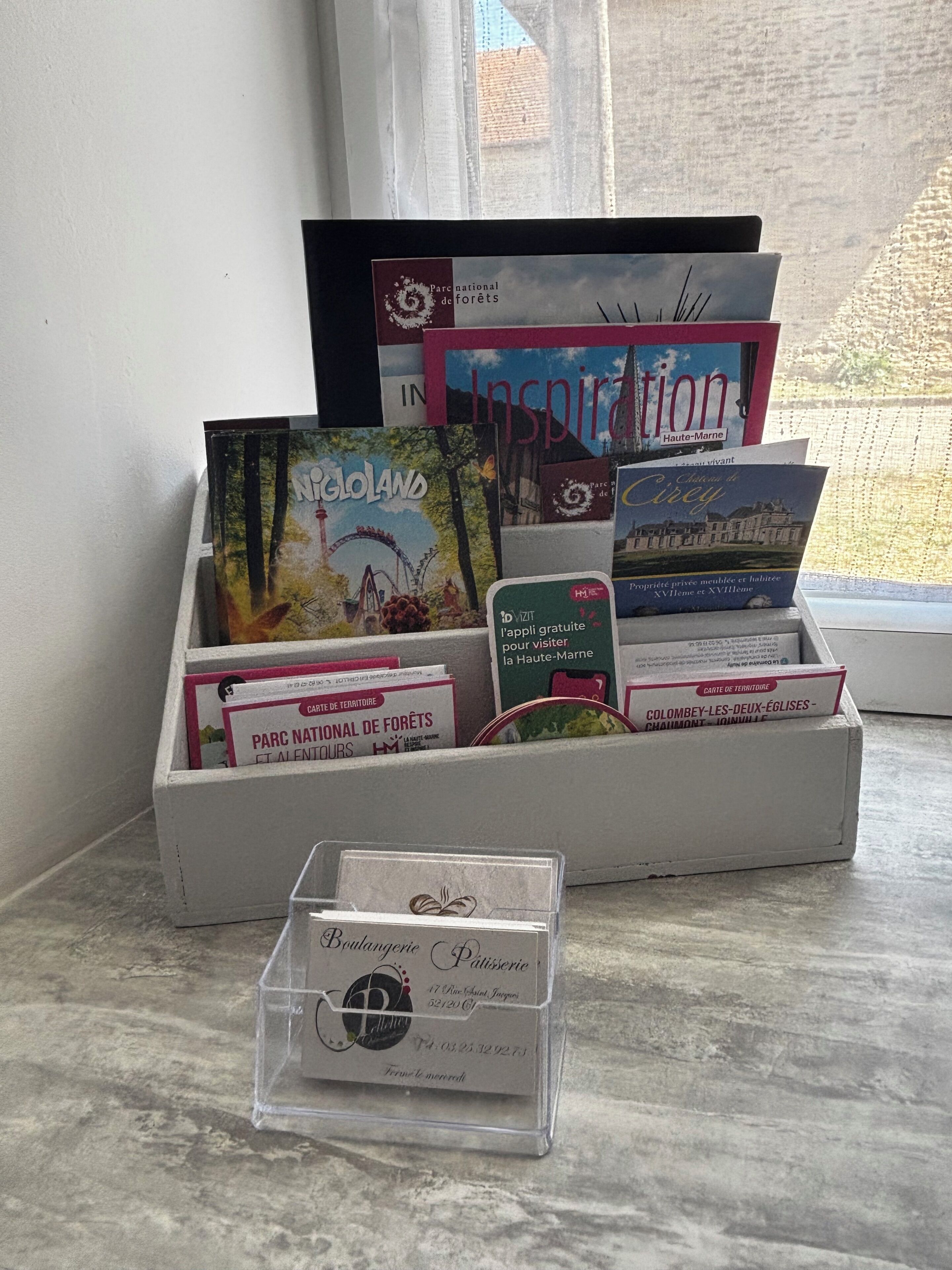 Une pile de brochures de voyage et une carte de visite sont posées sur une table près d’une fenêtre.