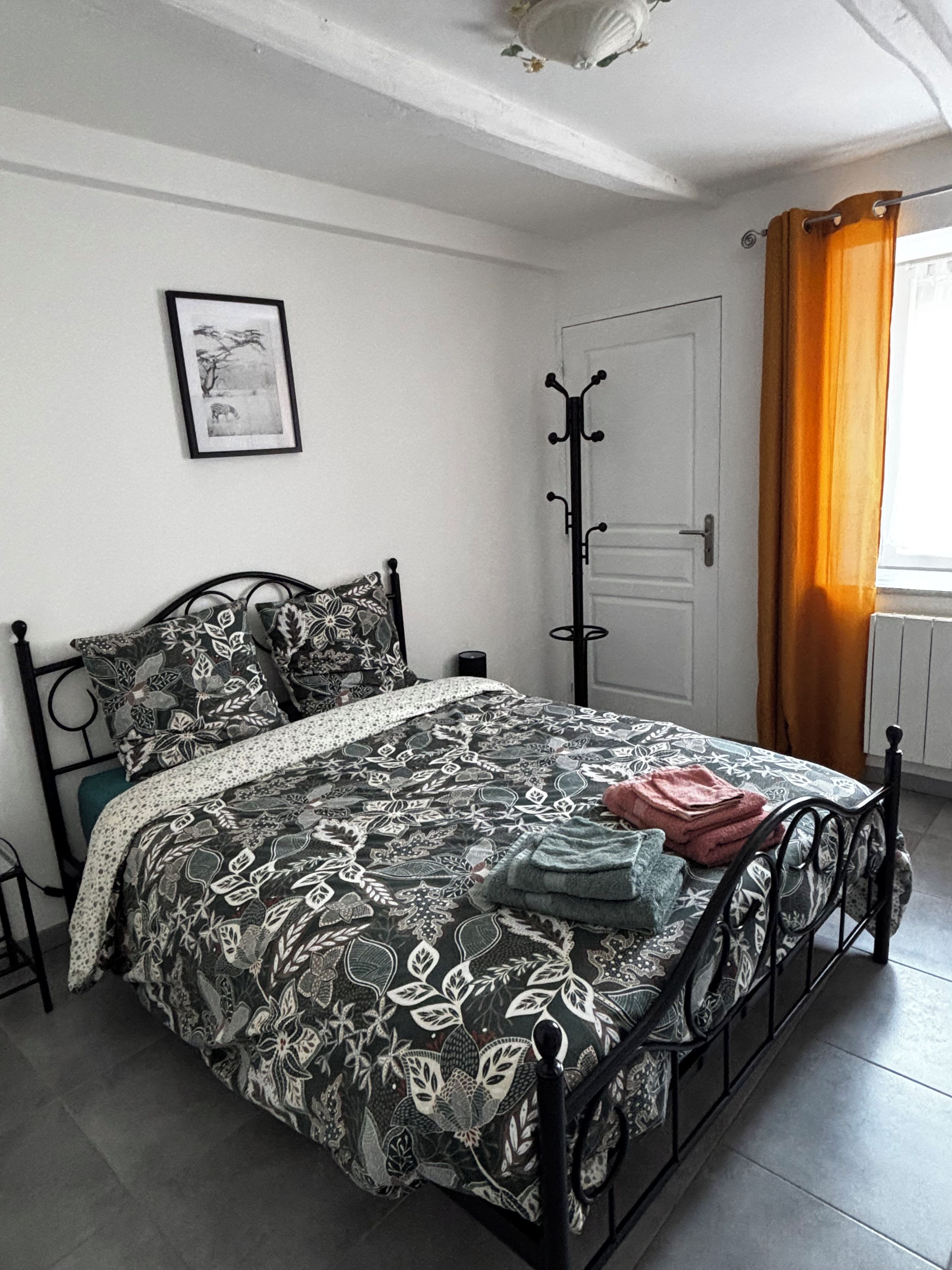 Un dormitorio con cama, perchero, puerta y ventana con cortinas.