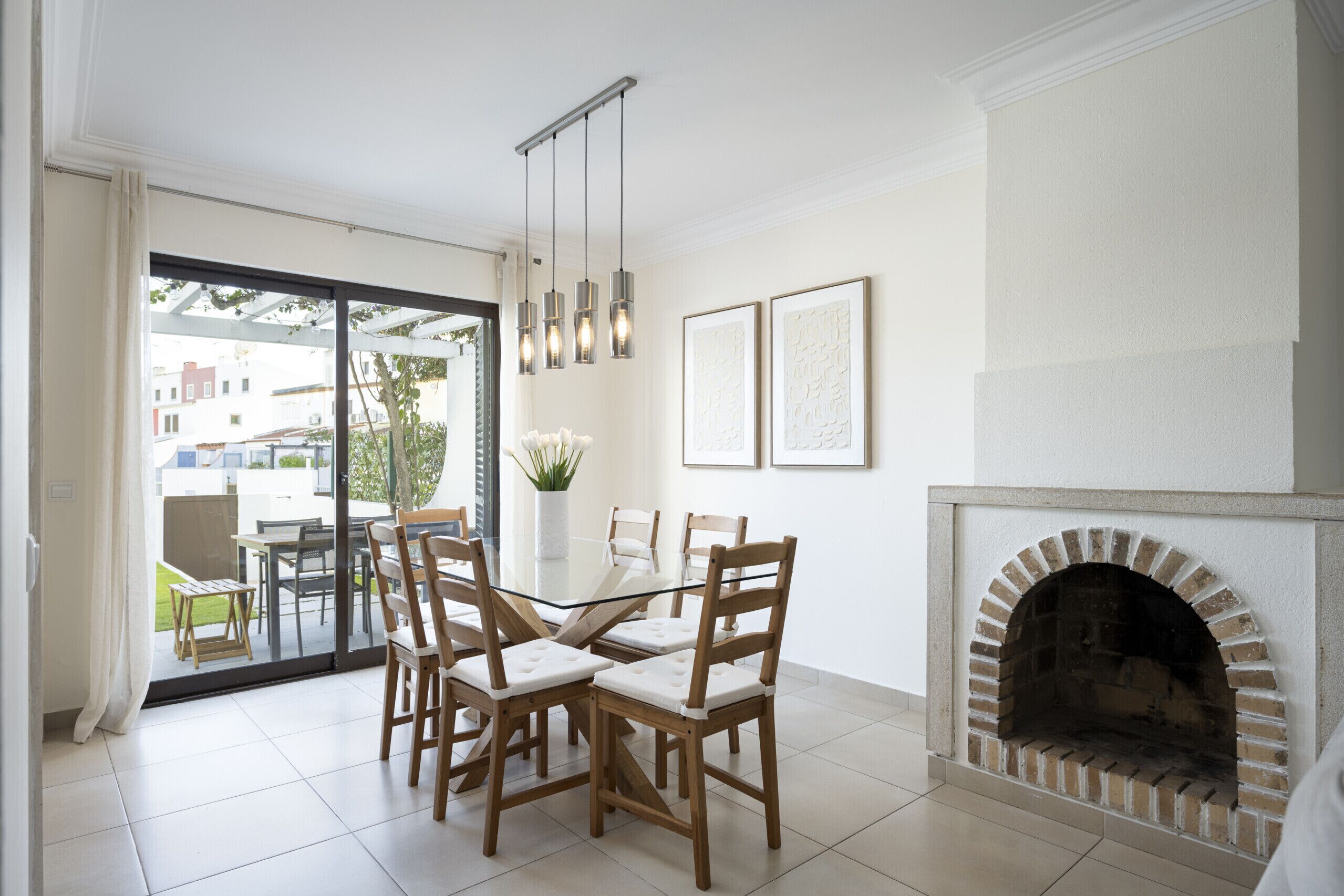 A dining area with a glass table, wooden chairs, a brick fireplace, and a view through a glass door to the outside.