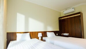 A hotel room with two beds, a wooden headboard, an air conditioning unit, and a nightstand with a lamp.