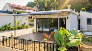 A modern house with a covered patio, a glass door leading to a room, and a garden with large leafy plants. - Family Room with Lake View (Hà Nội)