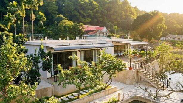 A modern building with a pool, surrounded by lush greenery and a hilly backdrop. - Family Room with Lake View (Hà Nội)