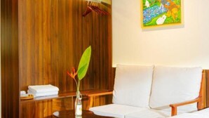 A hotel room with a bed, a seating area with a table, a painting on the wall, and a wooden wardrobe. - Family Room with Lake View (Hà Nội)