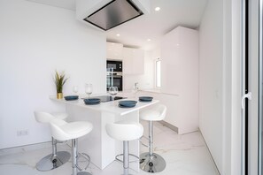 Eine moderne Küche mit weißen Schränken, einer zentralen Kochinsel mit Barhocker und einem eingebauten Backofen.