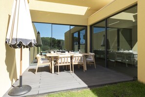 An outdoor dining area with a wooden table and chairs, a glass partition, and a patio umbrella. - Vilamoura Parque - Luxury Villa with pool by HD (Vilamoura)