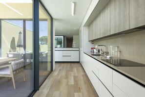 A modern kitchen with white cabinets, a black countertop, and a dining area with wooden furniture. - Vilamoura Parque - Luxury Villa with pool by HD (Vilamoura)
