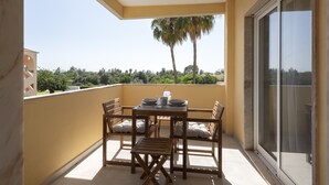 A balcony with a table and chairs, a sliding glass door, and a view of trees and greenery.