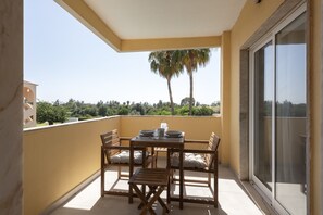Ein Balkon mit Tisch und Stühlen, eine Schiebetür und Blick auf Bäume und Grünflächen.