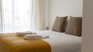A neatly made bed with a yellow bedspread, two pillows, and folded towels on the side.