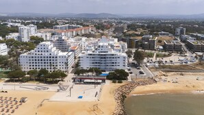 Eine Küstenstadt mit modernen Gebäuden, einem Strandabschnitt mit Sonnenschirmen und einem Beachvolleyballfeld.