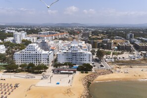 A coastal cityscape with modern buildings, a beach area with umbrellas, and a volleyball court. - Oceanides - Sea front with pool by HD (Quarteira)