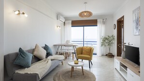 Ein Wohnzimmer mit Sofa, Sessel, TV-Schrank und einem Essbereich mit Tisch und Stühlen.