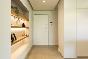 A hallway with a white door, wooden shelves, a small plant, and a thermostat on the wall. - The Five - Luxury apartment by HD (Quarteira)