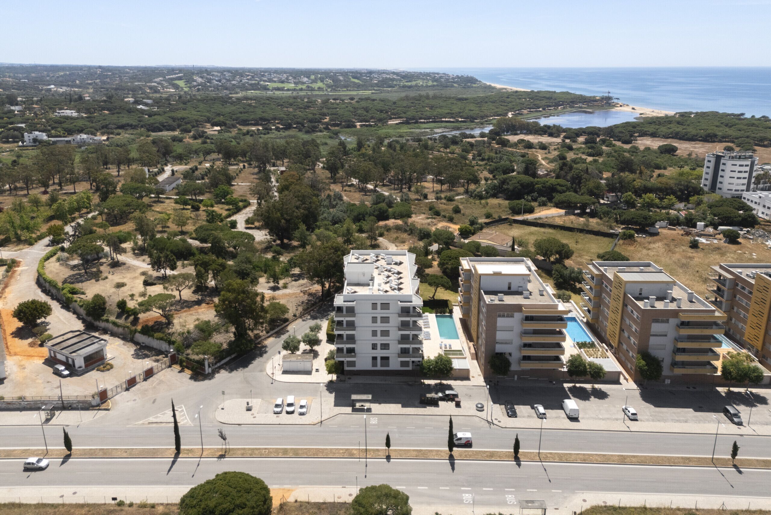 Vue aérienne d’une zone urbaine côtière, où l’on aperçoit un immeuble imposant à plusieurs étages, doté de balcons, d’une piscine et d’un parking.