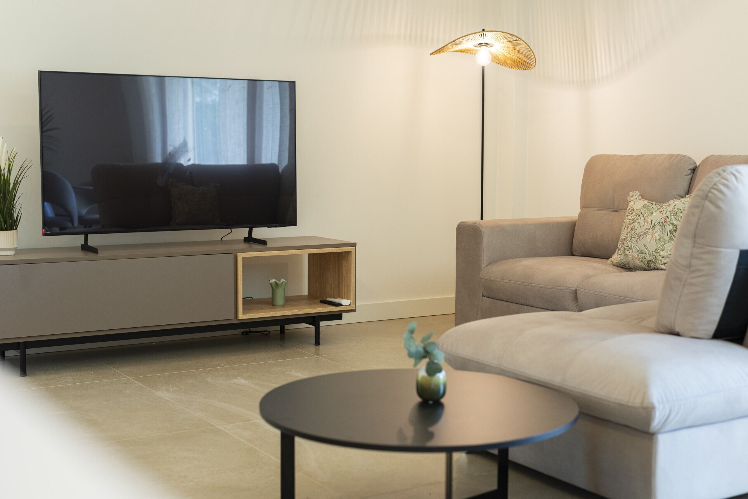 Een moderne woonkamer met een flatscreen televisie, een bank, een salontafel en een vloerlamp.