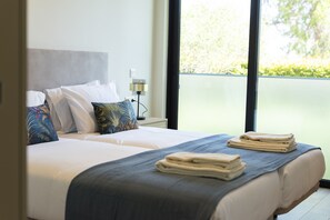 A hotel room with two beds, a nightstand with a lamp, and a view of greenery outside. - The Five - Luxury apartment by HD (Quarteira)