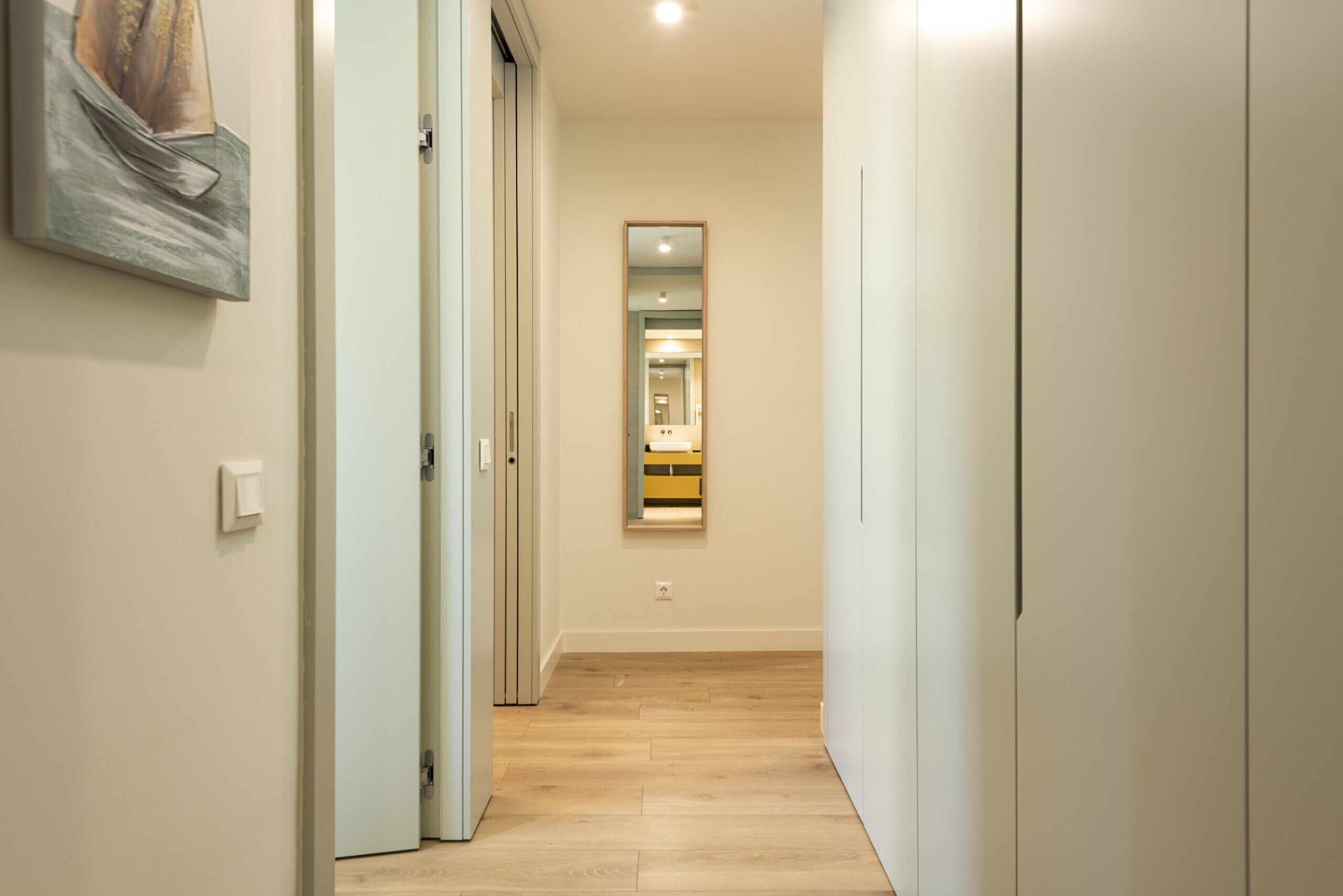A hallway with wooden flooring, a door on the left, and a mirror on the right.