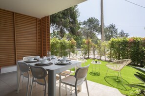 A patio with a table set for dining, surrounded by chairs, with a view of a well-maintained lawn and trees. - The Five - Luxury apartment by HD (Quarteira)