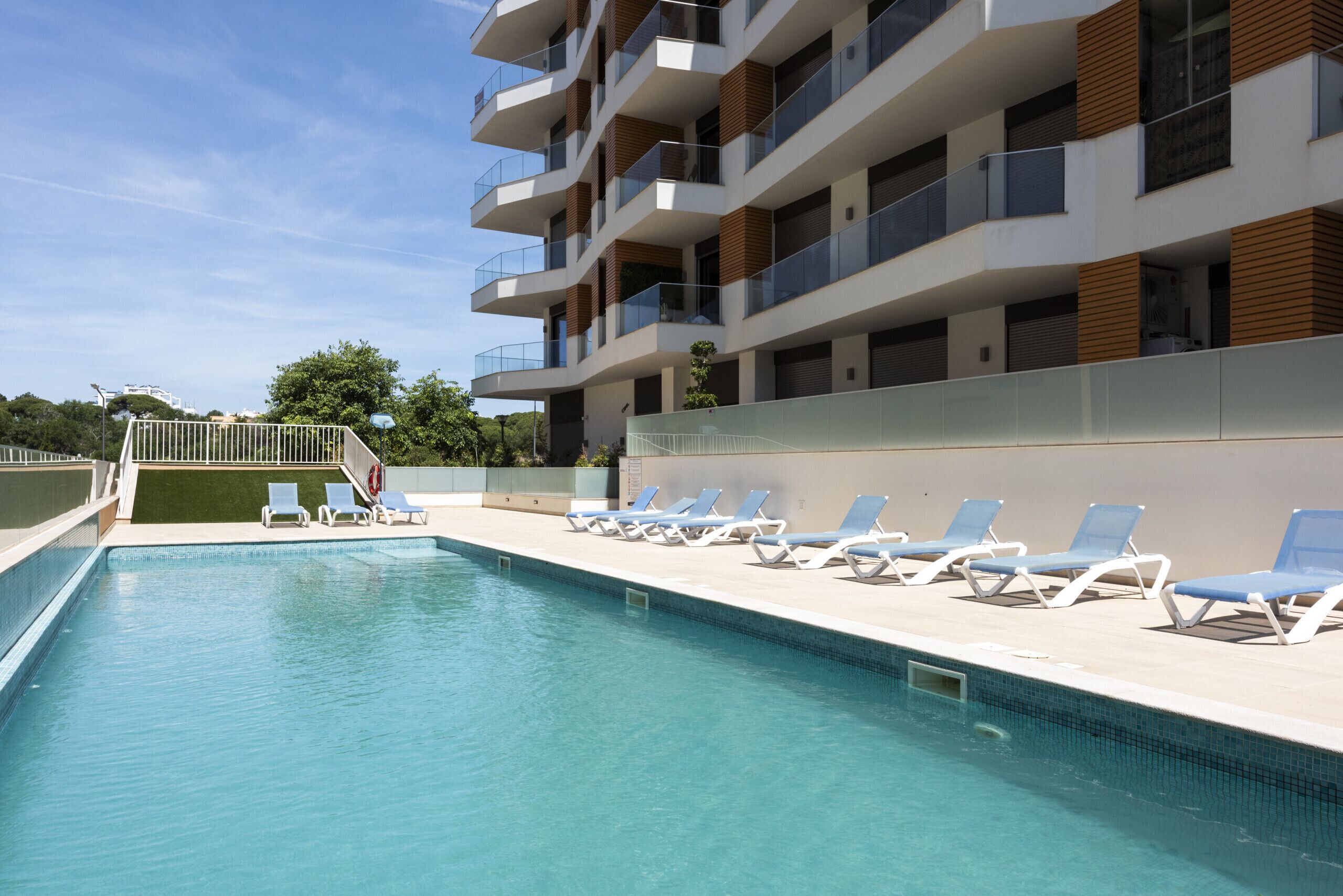 A swimming pool with lounge chairs and a modern building with balconies.