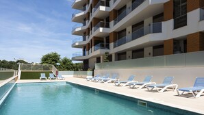 En swimmingpool med liggestole og en moderne bygning med altaner.