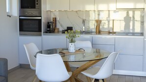 Une cuisine moderne avec des meubles blancs, des appareils en acier inoxydable et une table à manger en verre, assortie de chaises blanches.