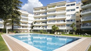 Une piscine entourée d’un immeuble à plusieurs étages doté de balcons, d’une pelouse et sous un ciel dégagé.
