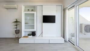 Un salon moderne doté d’un meuble de rangement intégré pour les appareils multimédias, d’un téléviseur à écran plat, d’une plante en pot et d’une porte-fenêtre coulissante donnant sur un espace extérieur.