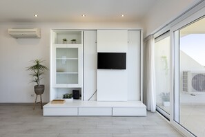Ein modernes Wohnzimmer mit einer eingebauten Unterhaltungsecke, einem Flachbildfernseher, einer Topfpflanze und einer Glastür, die zu einem Außenbereich führt.