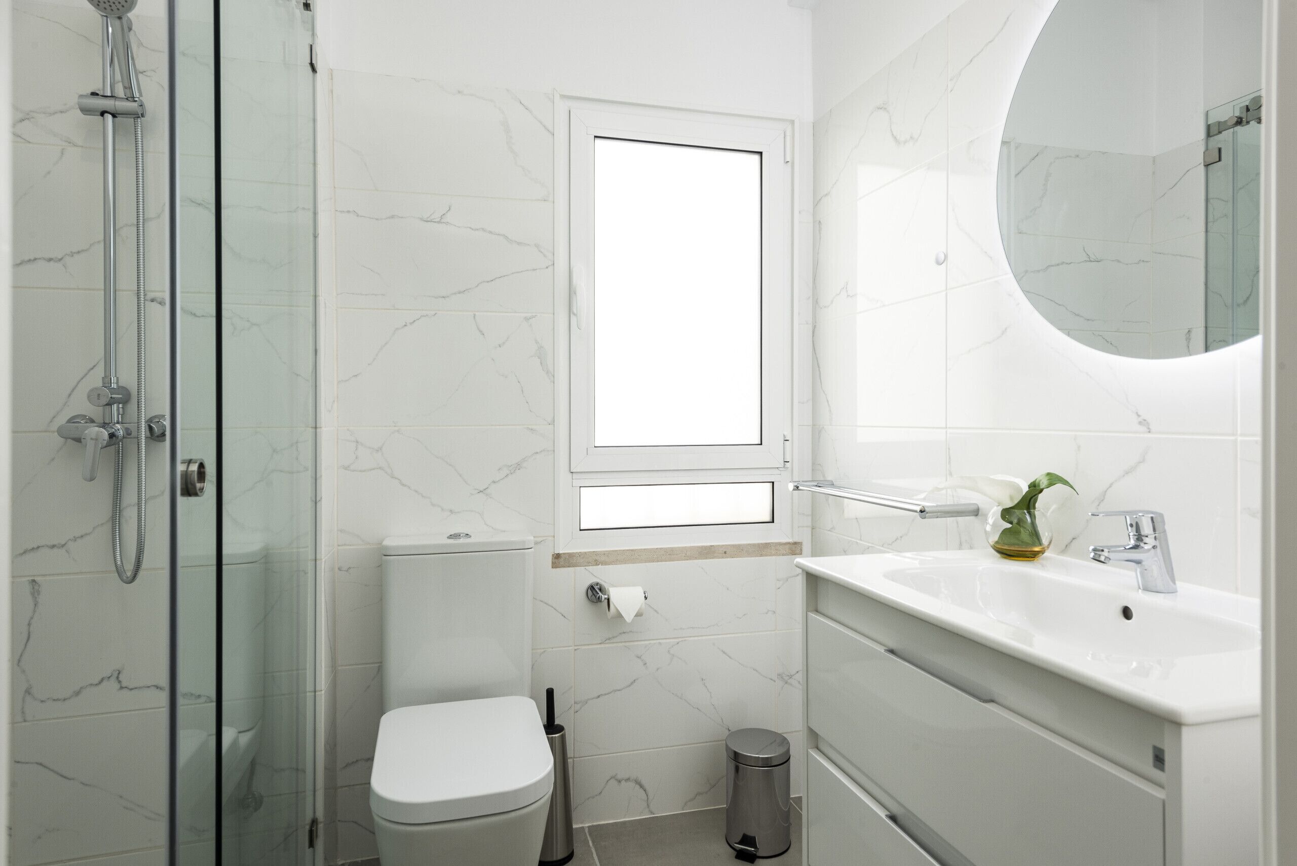 Een moderne badkamer met een douchecabine van glas, een toilet, een wastafel met spiegel en een kleine prullenbak.