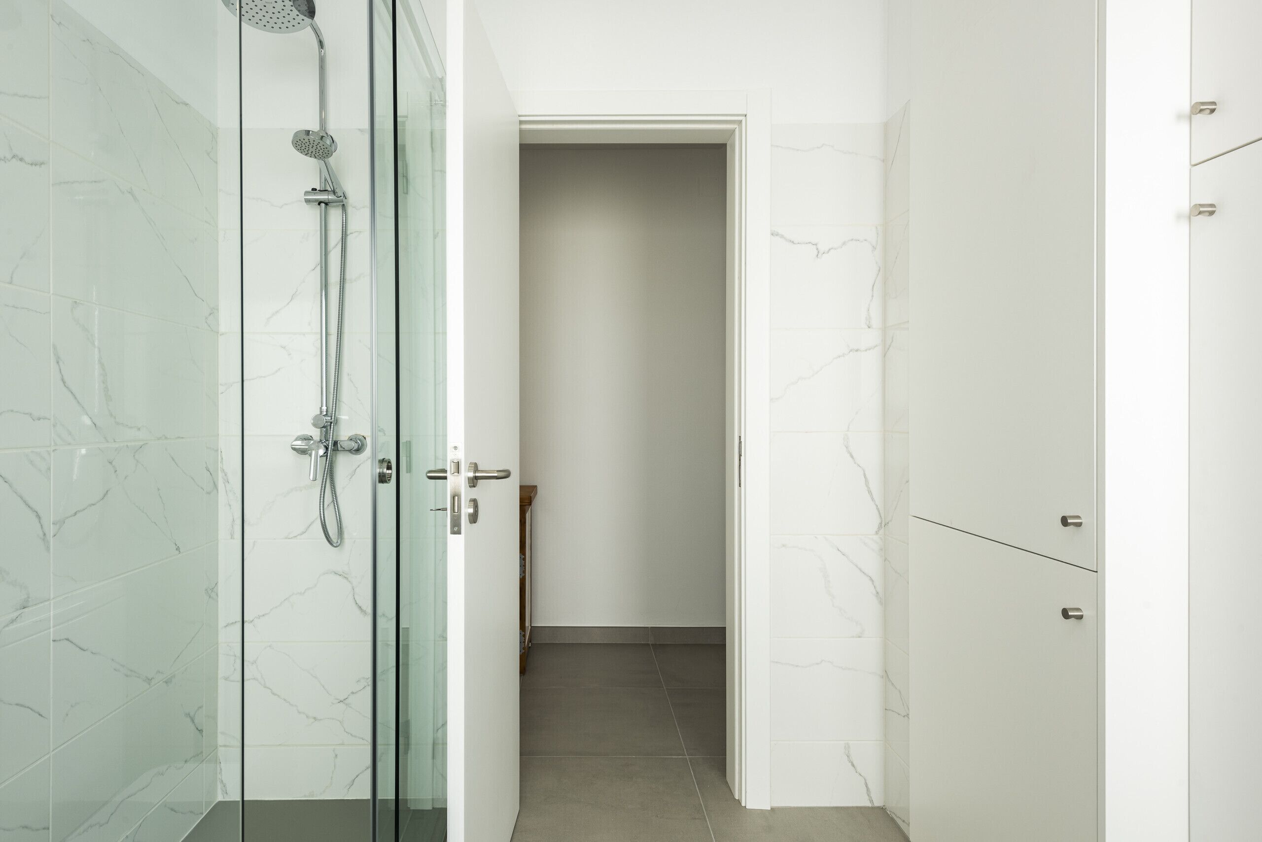 A modern bathroom with a glass-enclosed shower, a white door leading to a hallway, and a marble-tiled wall.