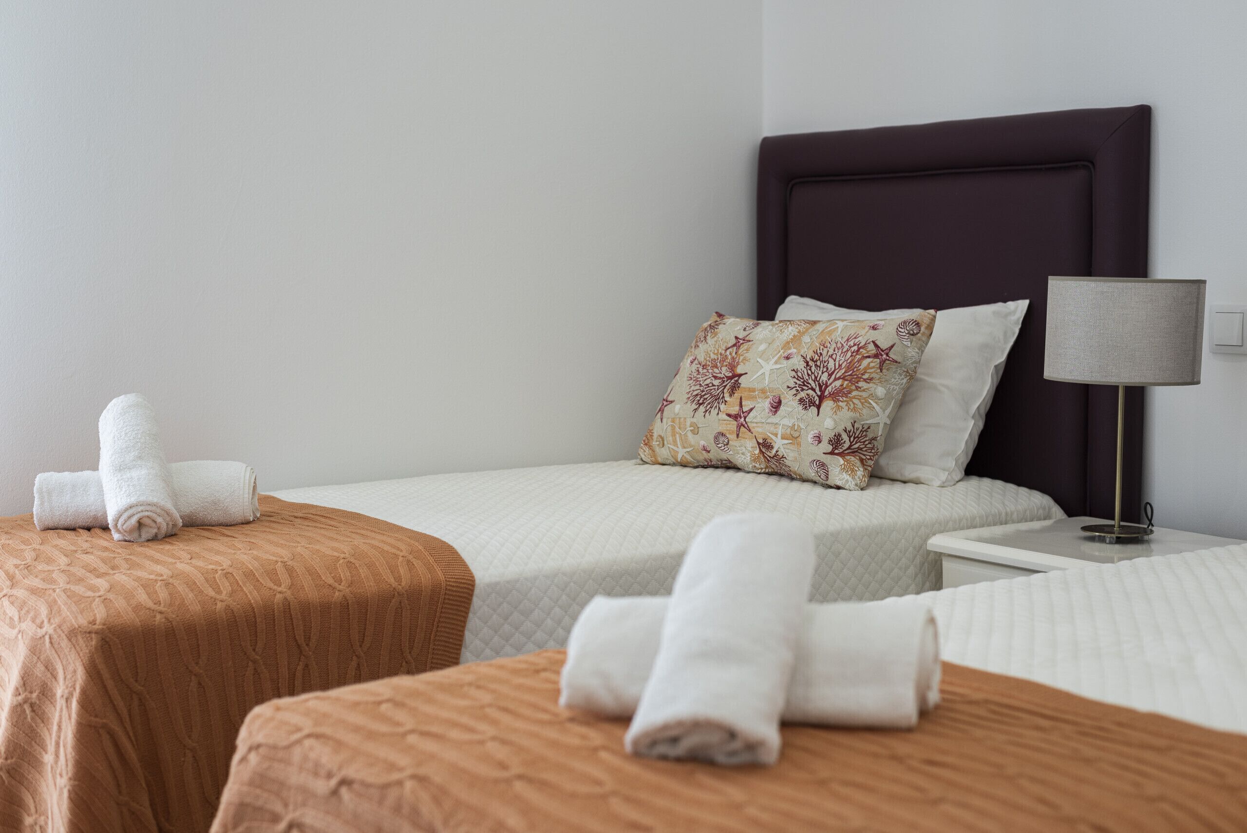 Une chambre d’hôtel avec deux lits, une table de chevet avec une lampe et des serviettes soigneusement pliées.