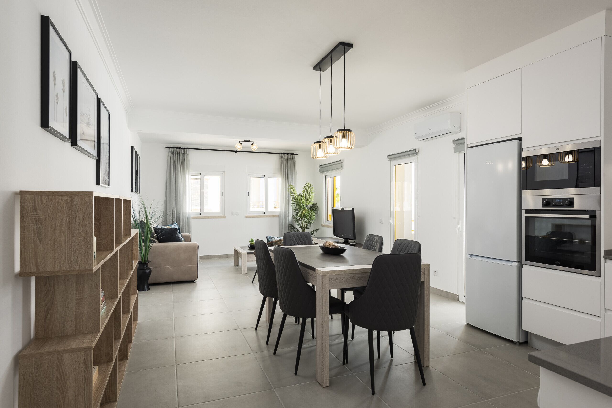 A modern kitchen with white cabinets, a dining table, and chairs. There is a TV and a plant on the table.