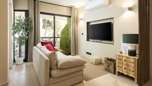 Een moderne woonkamer met een bank, een flatscreen televisie, een klein houten bijzettafeltje en een potplant.