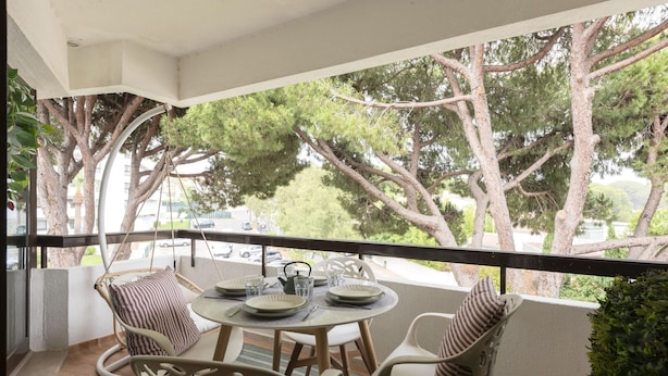 Een balkon met een ronde tafel voor vier personen, omringd door rieten stoelen, met uitzicht op een straat met bomen.