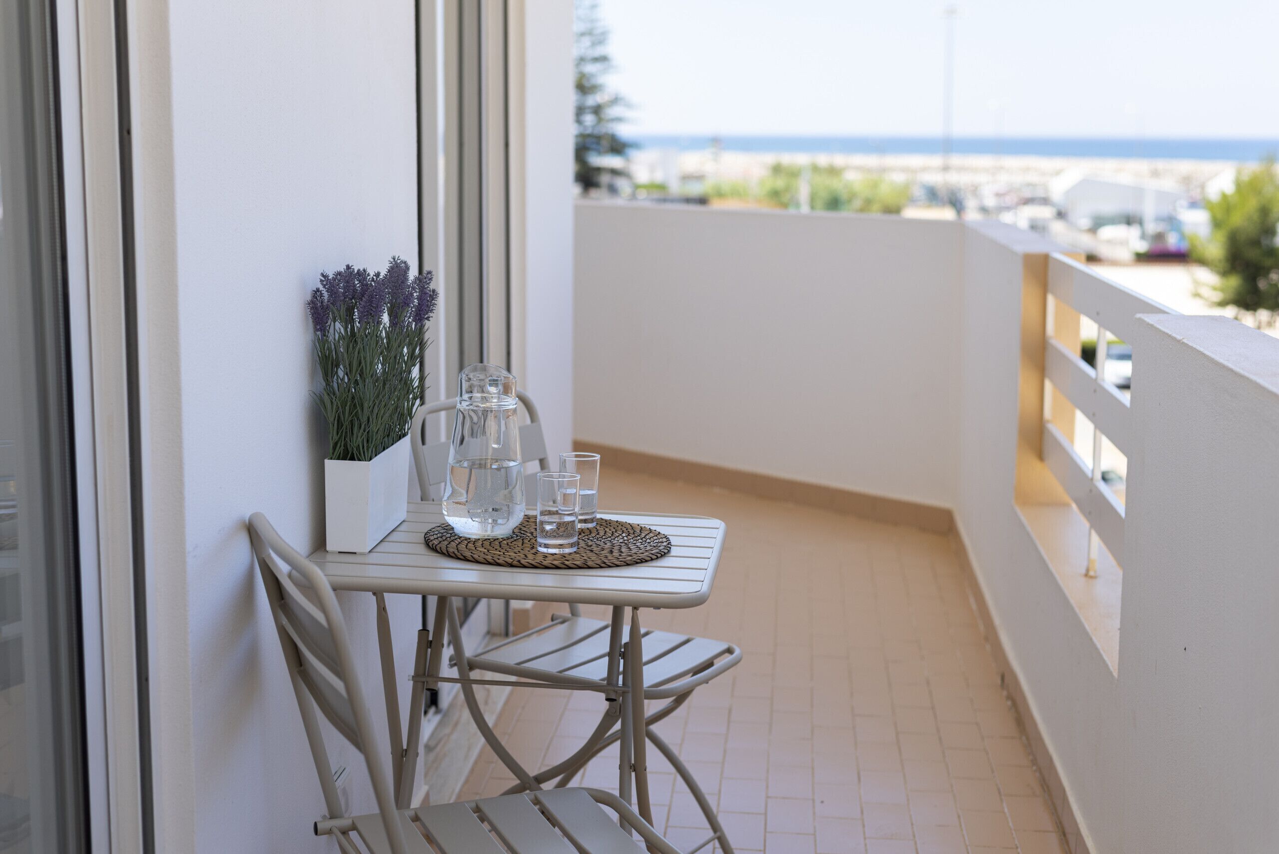 Un balcón con una mesa, sillas, una planta en maceta y vista al mar.