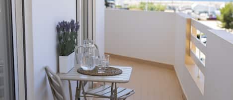 A balcony with a table, chairs, a potted plant, and a view of the sea.