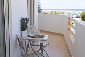 A balcony with a table, chairs, a potted plant, and a view of the sea. - Espadarte - Sea view by HD (Quarteira)