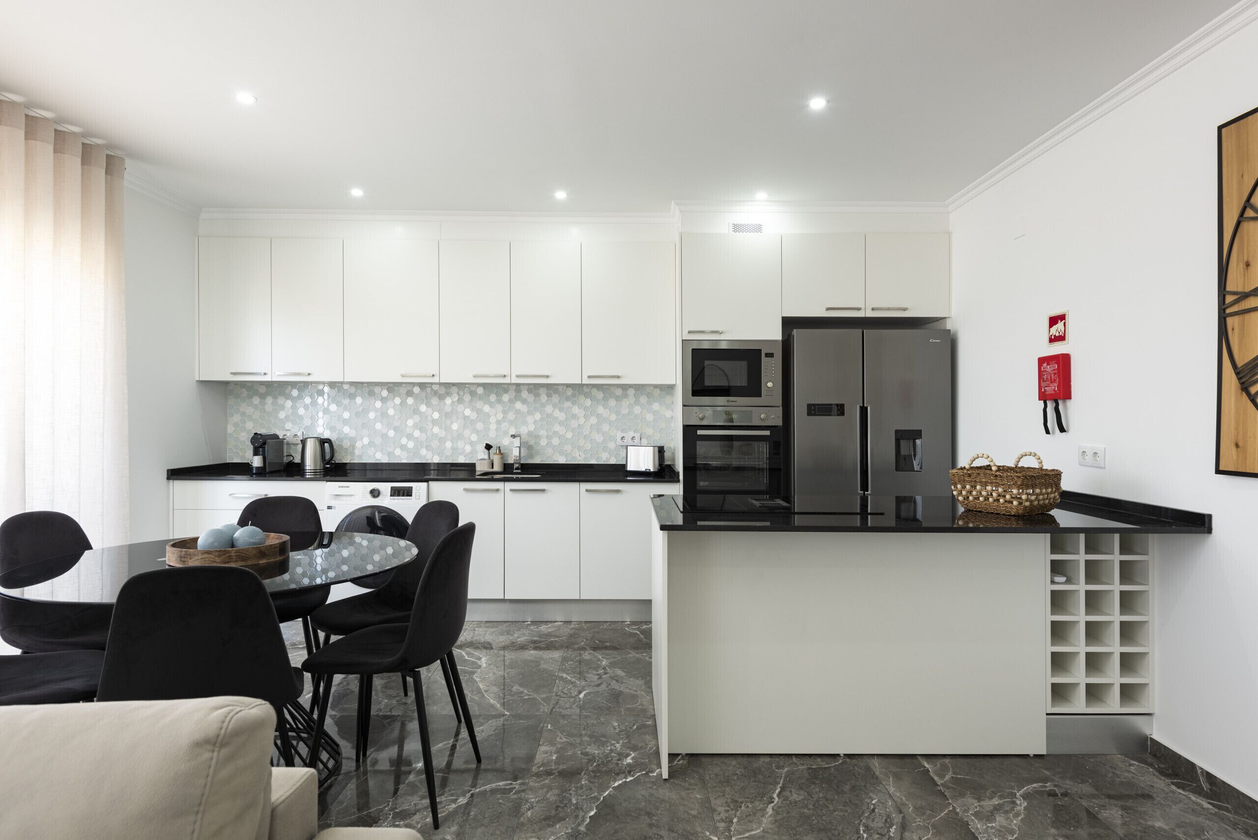 A modern kitchen with white cabinets, a black countertop, and a dining area with a round table and chairs.