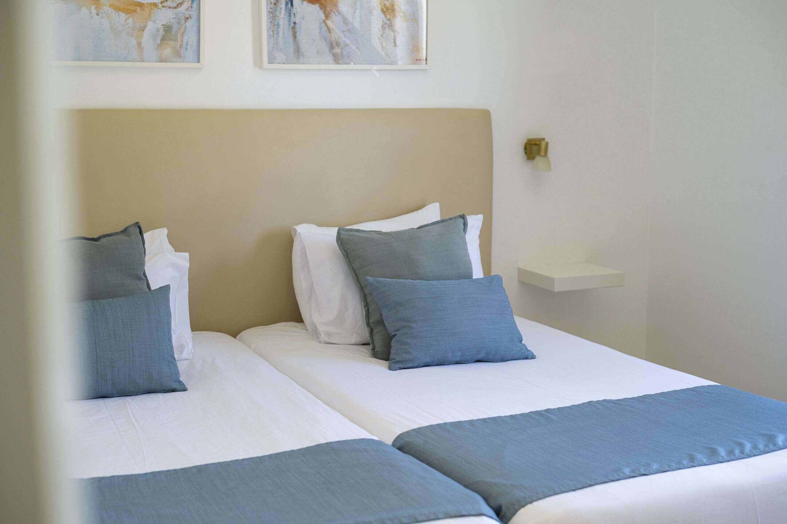 Una cama doble con cabecera color beige, dos almohadas y una manta azul.