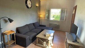Una sala de estar con sofá, mesa de centro, lámpara, reloj y ventana.
