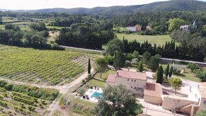 Viñedo con hileras de vides, una piscina y edificios tradicionales con tejados de tejas rojas.