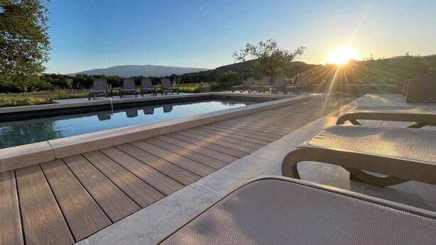 Una piscina con sillones de descanso, una terraza de madera y vistas al paisaje.