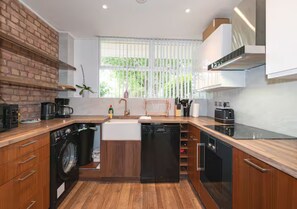 Eine moderne Küche mit Holzschränken, einer eingebauten Waschmaschine, einem Geschirrspüler und einem Fenster mit Jalousien.