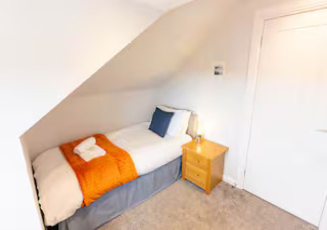 Une petite chambre avec un lit simple, un plafond en pente, une table de chevet et une commode.