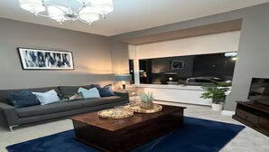 Uma sala de estar com uma mesa de centro de madeira escura, um tapete azul, um sofá cinza com almofadas e um candelabro.