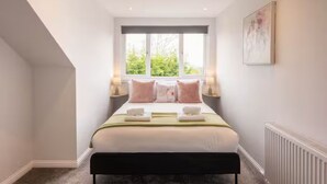 Quarto com cama, luminárias de cabeceira, janela e radiador.