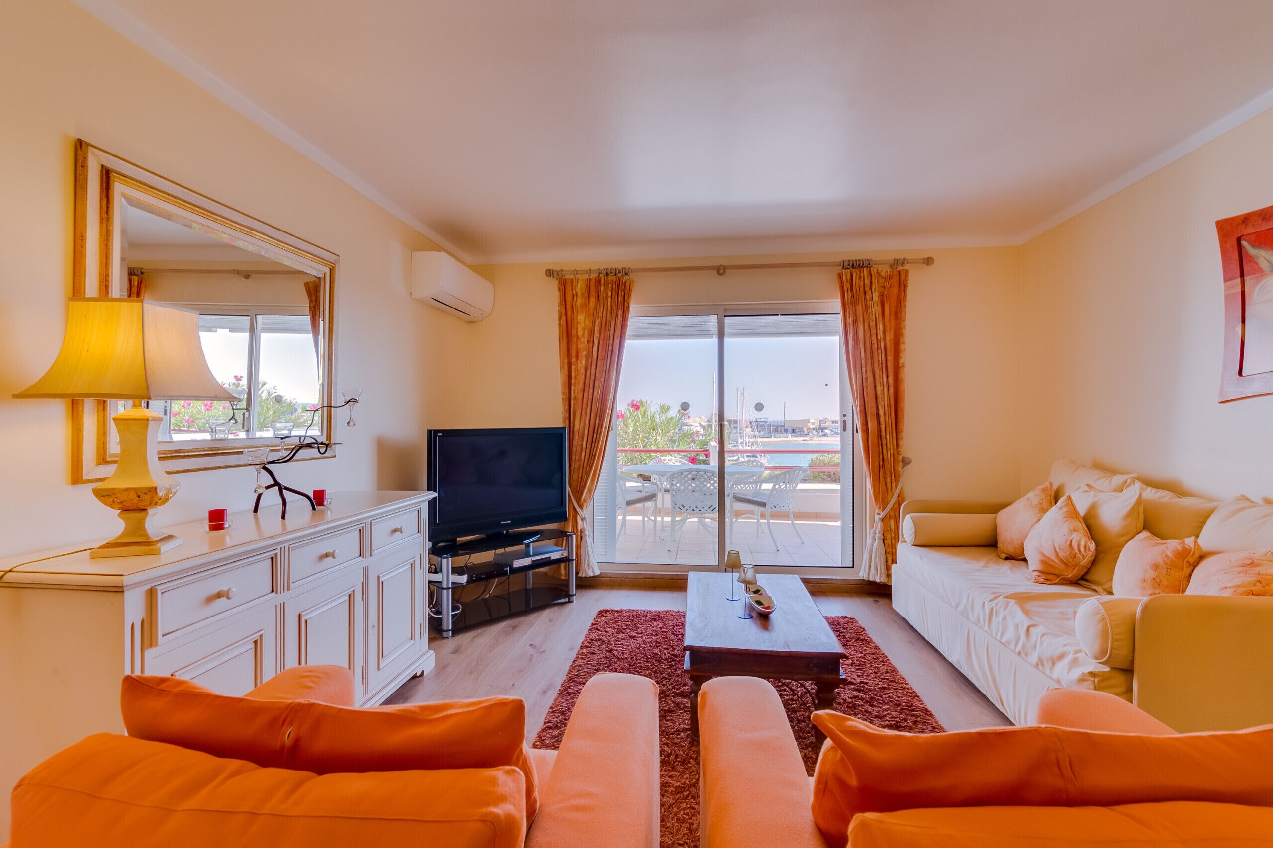 A living room with a television, sofa, and a view of the outdoors.