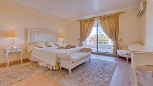 A bedroom with a large bed, two bedside tables with lamps, a sofa, a desk, and a view of the outdoors. - São Vicente - Vilamoura (Vilamoura)