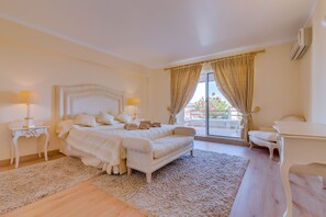 A bedroom with a large bed, two bedside tables with lamps, a sofa, a desk, and a view of the outdoors. - São Vicente - Vilamoura (Vilamoura)