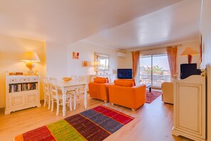A living room with a TV, orange sofas, a white dining table, and a colorful rug. - São Vicente - Vilamoura (Vilamoura)